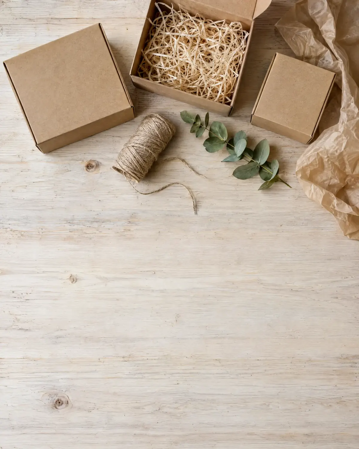 Cardboard boxes, a spool of twine and green leaves on a timber surface